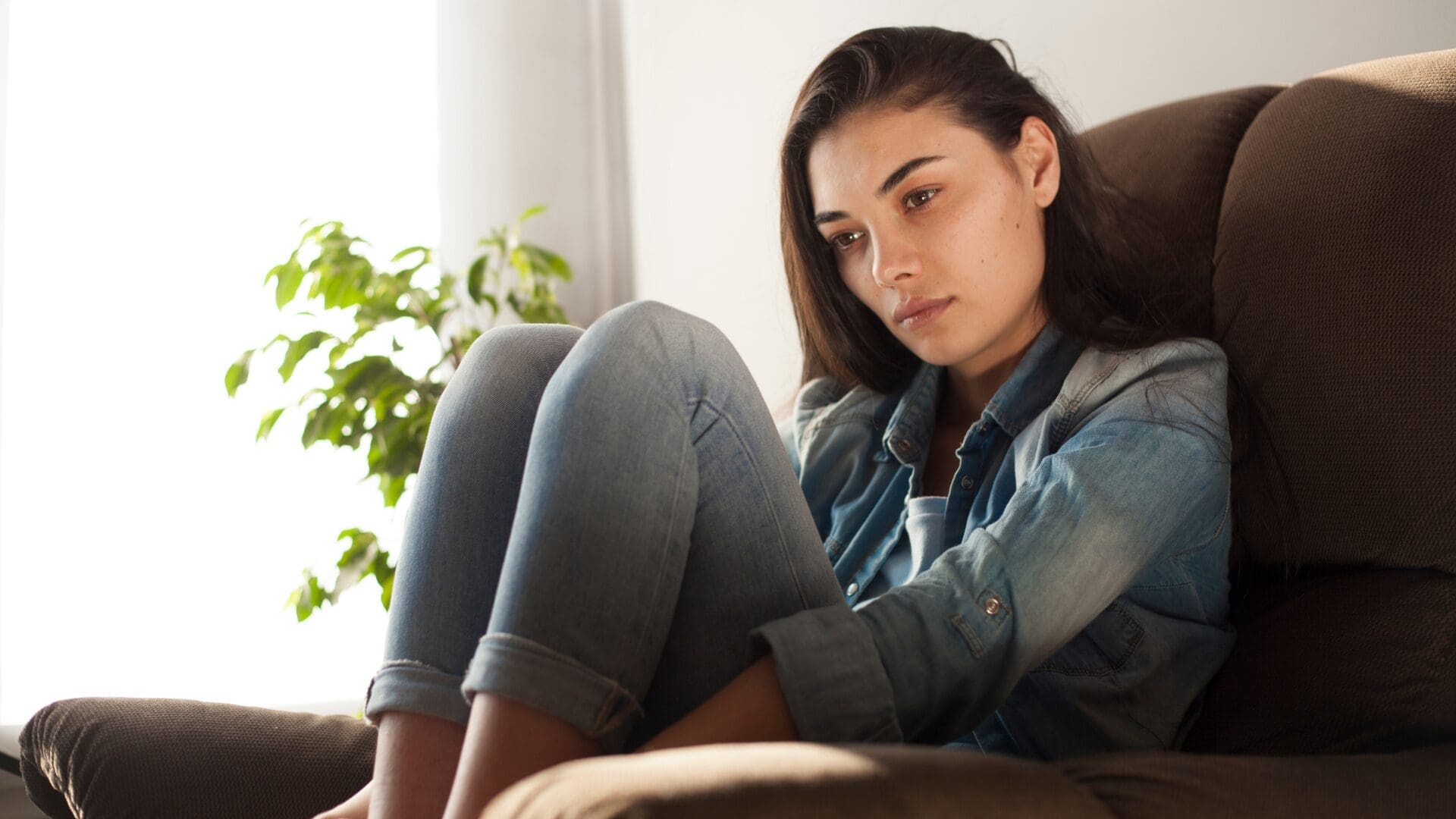 Woman sitting on a sofa in a thoughtful pose, looking inward as if reflecting or processing emotions.